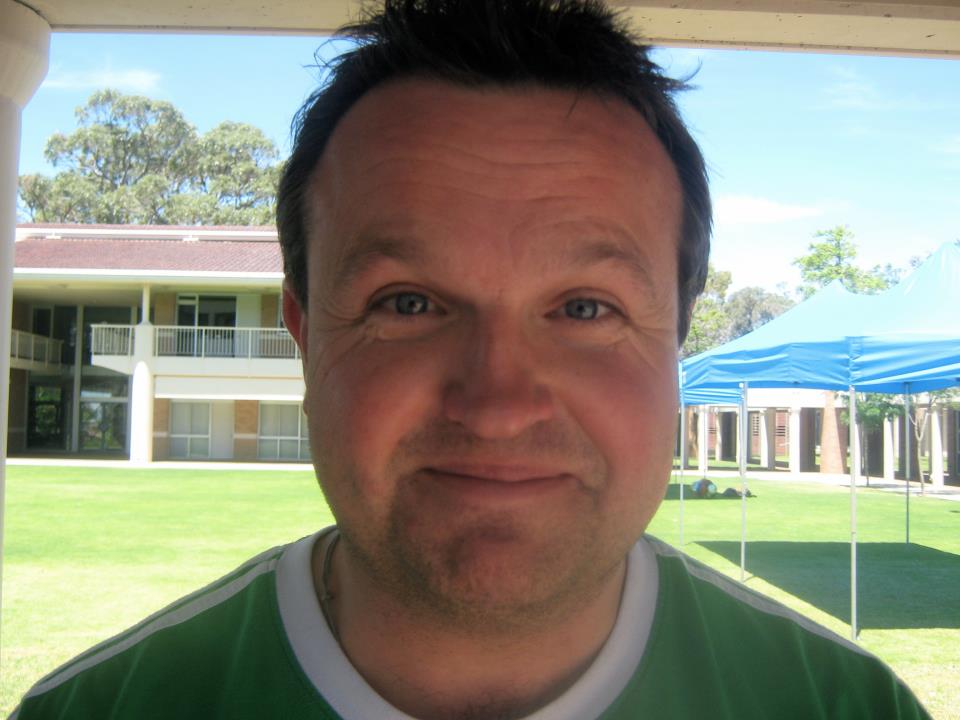 Photo of author Danny in front of a green lawn with buildings in the background. He's wearing a green shirt with a white collar.