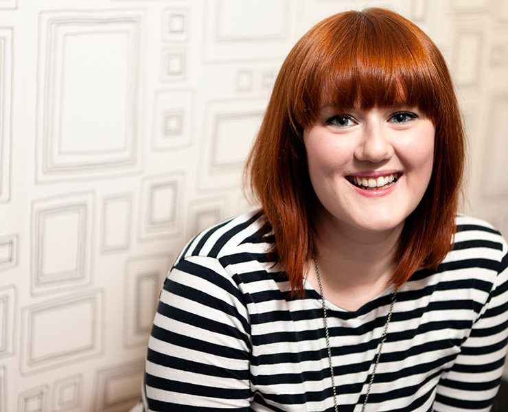 Author Lindsey Kelk in front of a white background with printed frames wearing a black and white striped long sleeve top