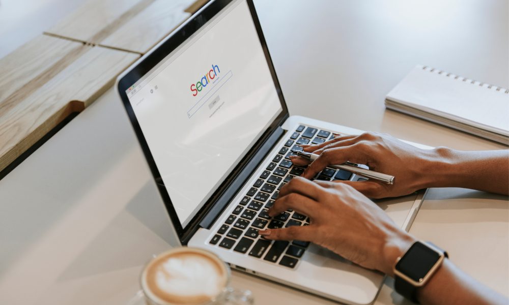 Hands holding a pen typing on a laptop on a search engine page.