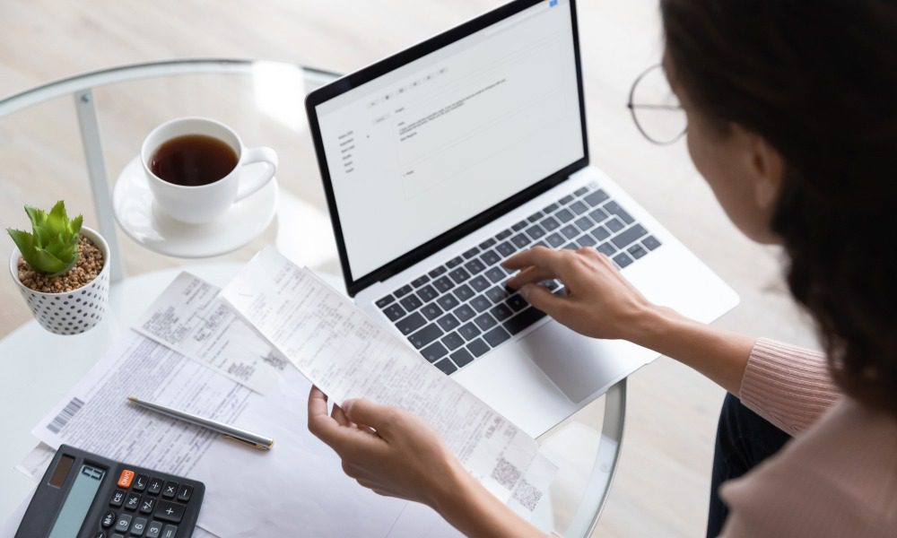  A woman looking through her receipts and using a laptop, with a calculator and coffee nearby.